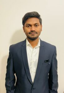 Image of editor Raju Kanukula. Raju is wearing a navy blazer with a white shirt with the top button open.