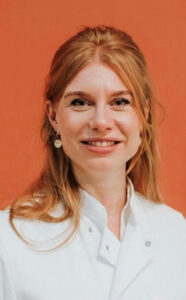 Image of blog author, Dr. Babette van Esch. Dr. Esch has red hair, and is wearing a white shirt. She is smiling showing her teeth. The background is orange and the photo is taken from the chest up.