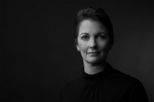 A black and white headshot of Gabrielle Brand, hair swept back, facing the viewer.