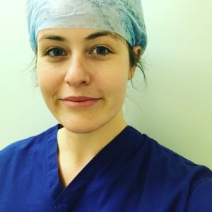 A head shot of the author wearing dark blue scrubs with surgery cap. She has dark brows and is smiling at the viewer.