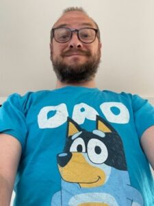 Photo of Matthew Doré wearing a blue t-shirt with Bluey character printed on the front.